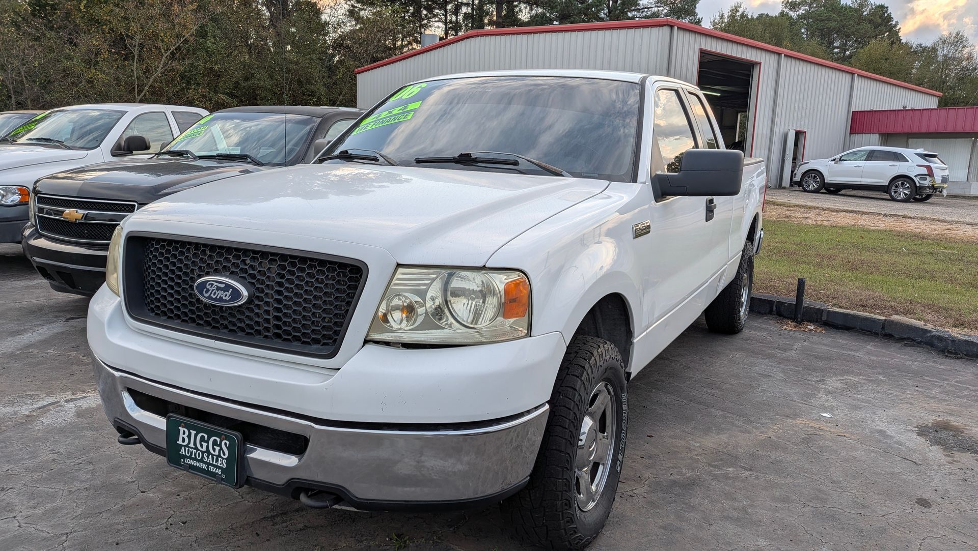 White Ford F-150 truck parked at a dealership, with other vehicles in the background.