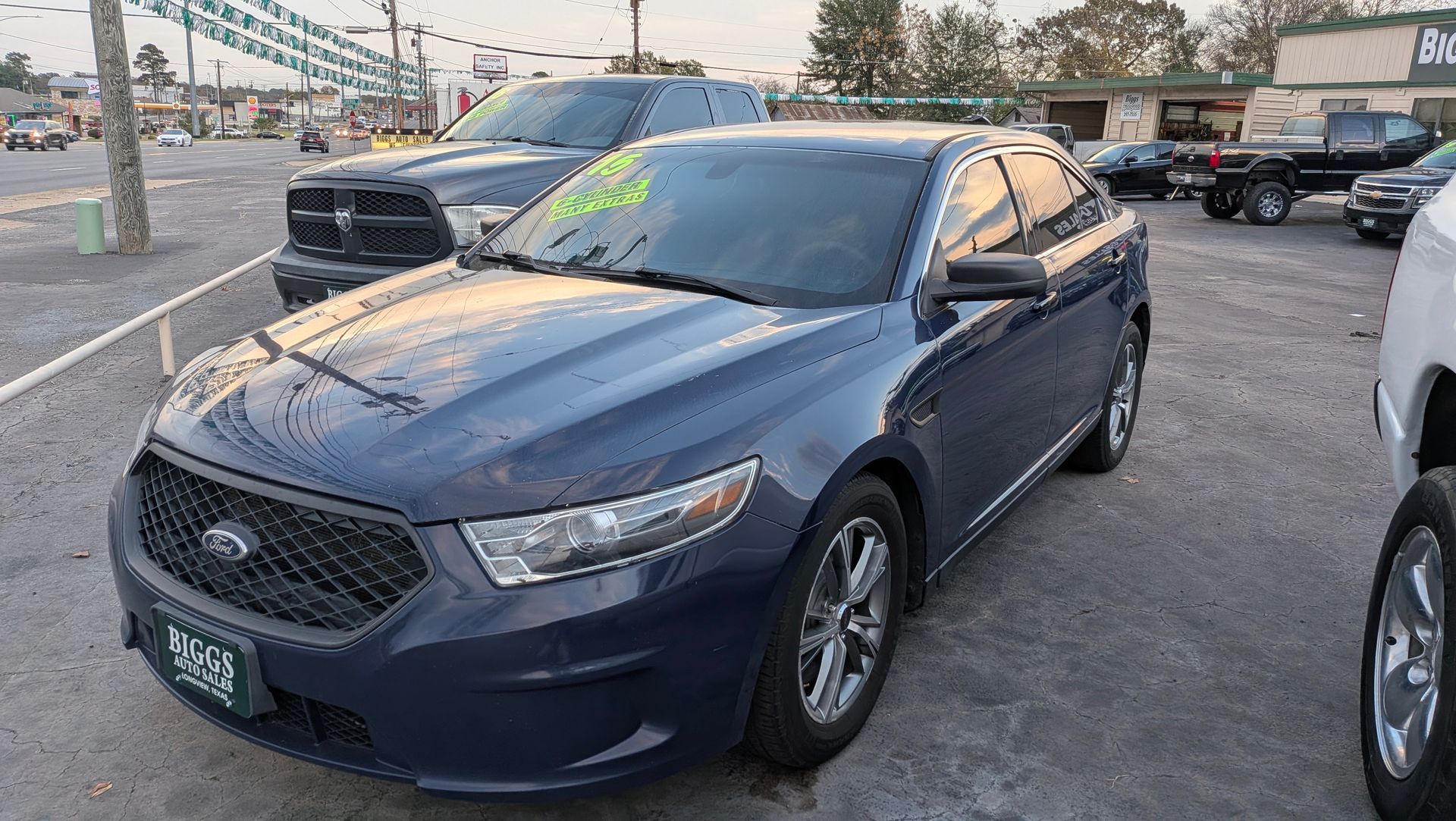 Blue Ford Taurus sedan at a car dealership lot; other vehicles visible.
