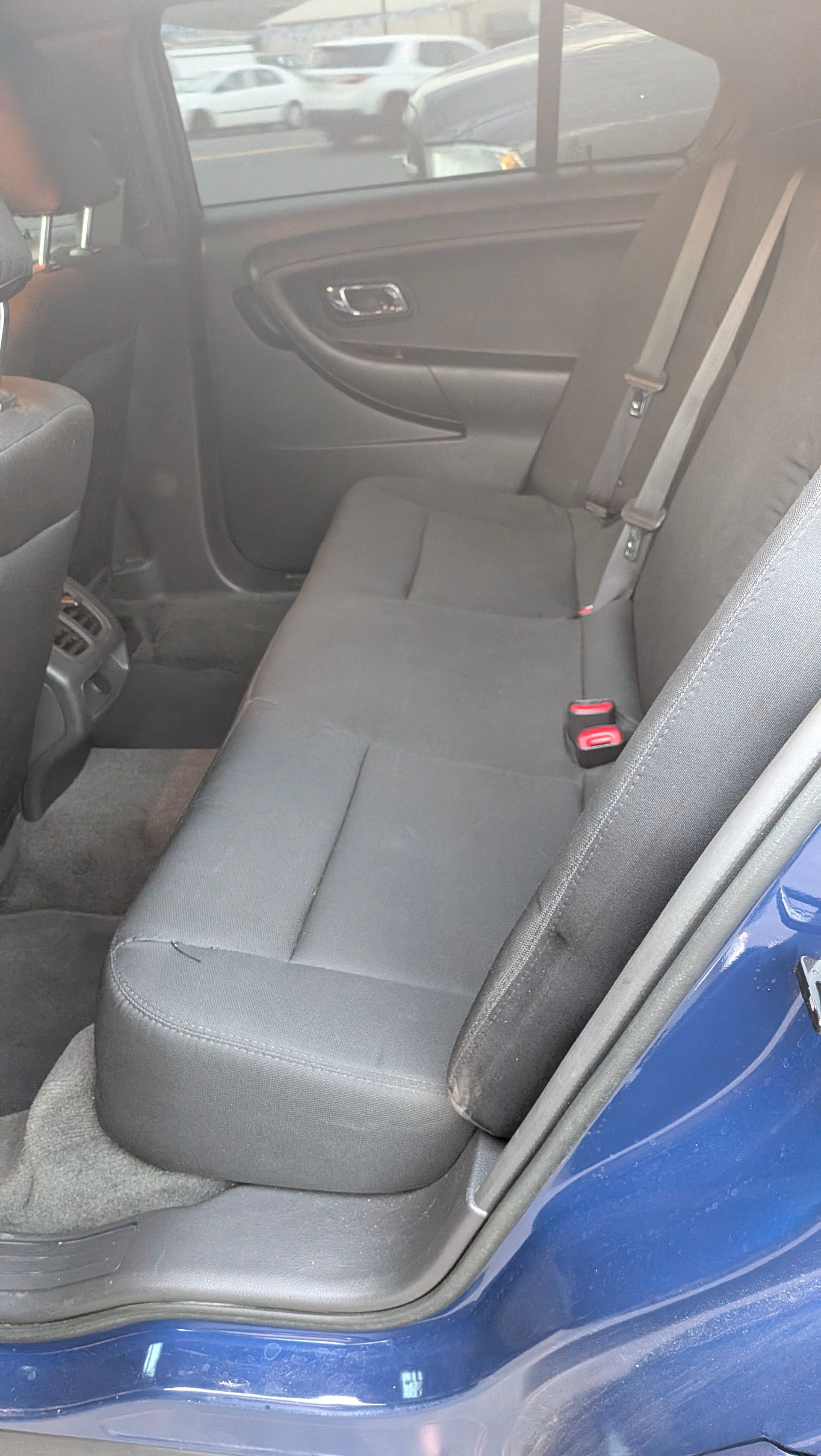 Blue car interior, rear seat. Black seats, seatbelts visible, parked outside.