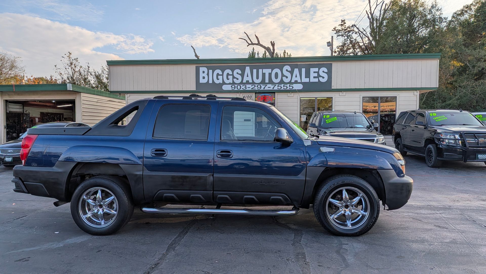 Blue Chevrolet Avalanche truck parked in front of Biggs Auto Sales building.