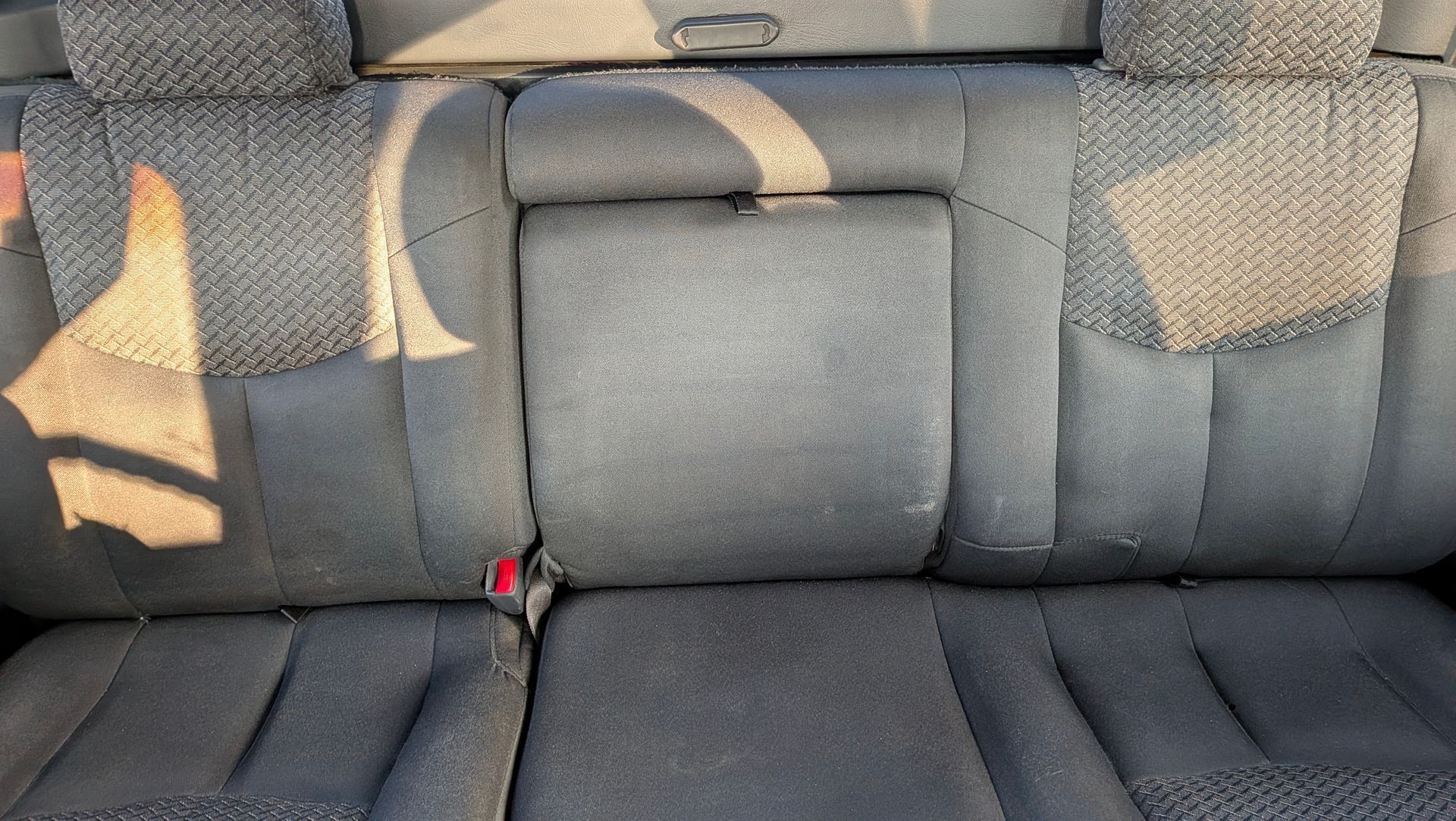 Gray car back seat with a fold-down center armrest, showing wear and tear on the fabric.