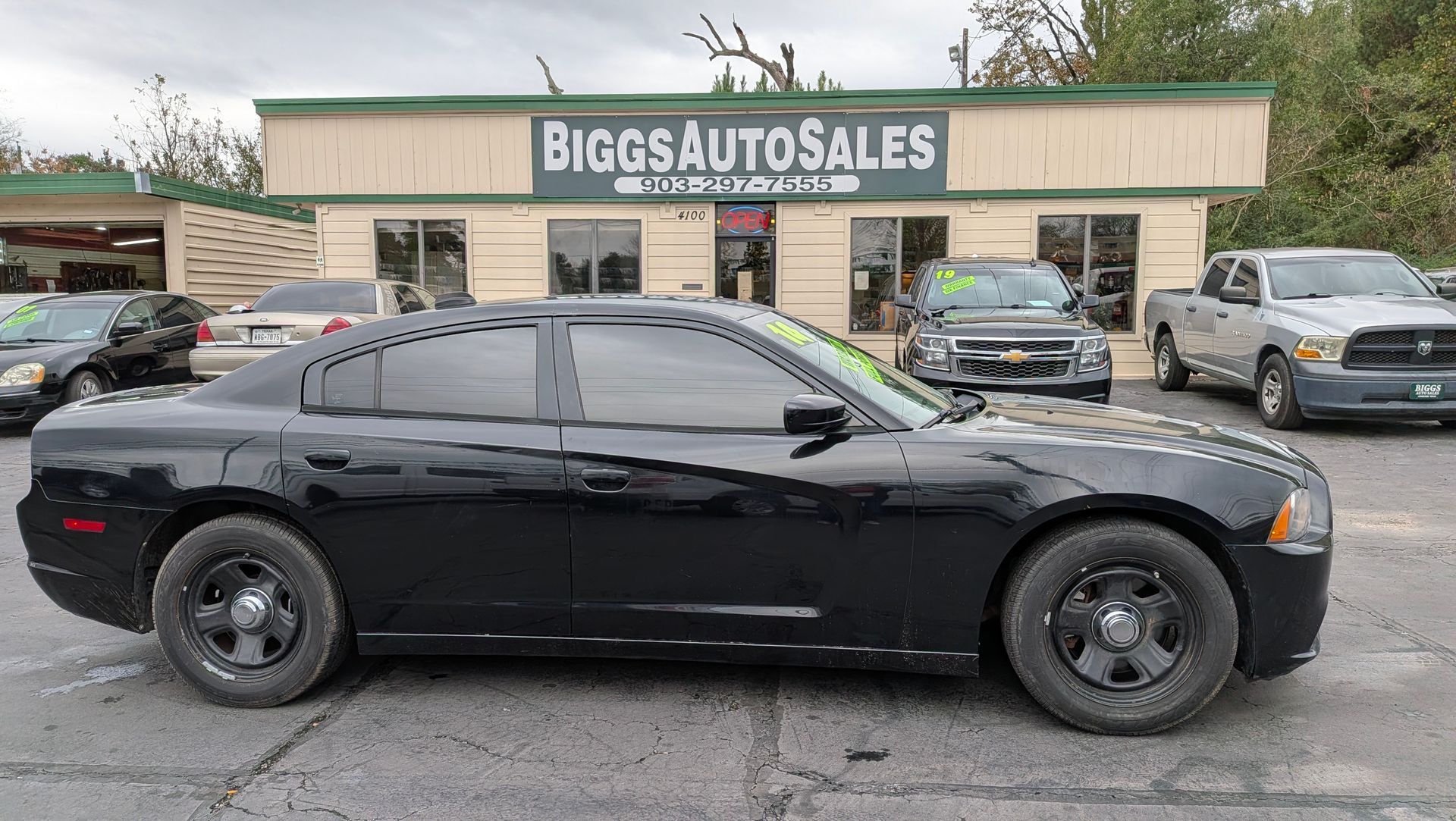 Black Dodge Charger police car parked in front of a car dealership, 