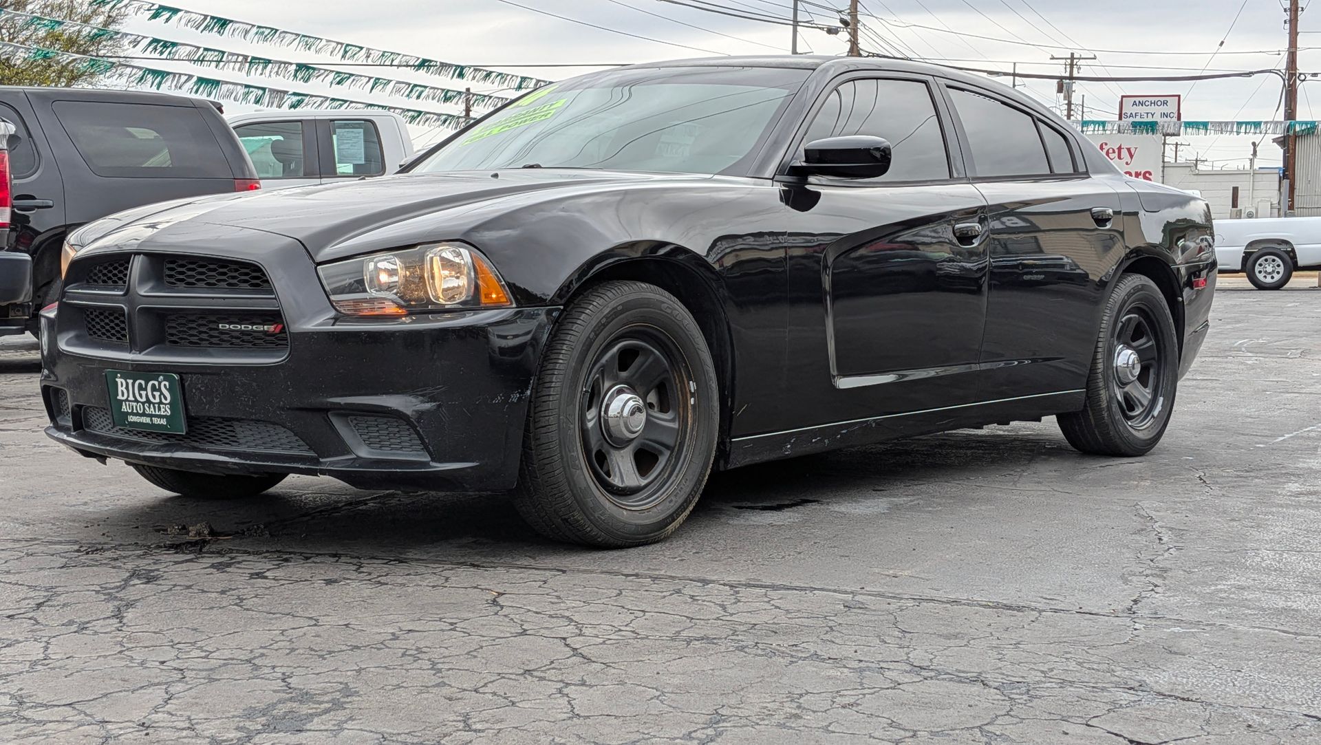 Black Dodge Charger police car parked outside on wet pavement.