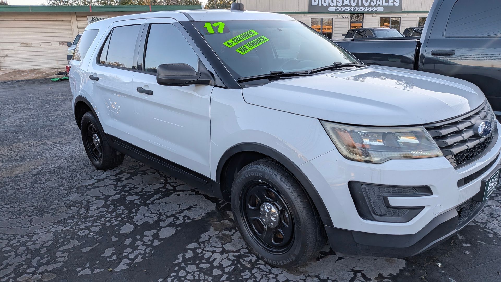 White 2017 Ford Explorer police SUV with black rims parked outside a car dealership.