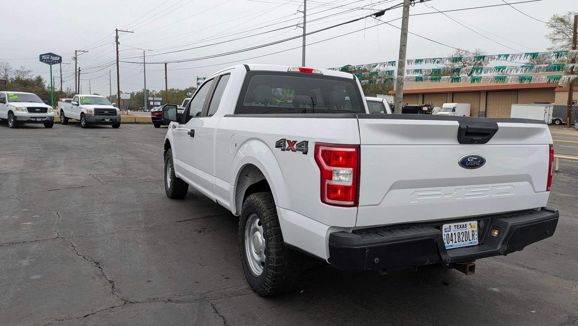 White Ford F-150 pickup truck parked on asphalt lot, with other trucks in the background on an overcast day.