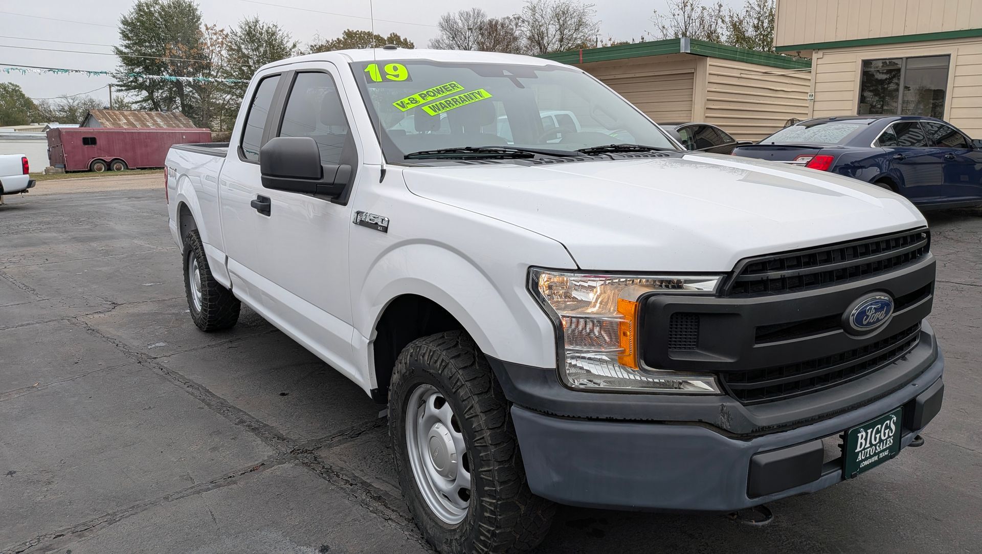 White Ford F-150 pickup truck parked on asphalt in front of a building; it has a 