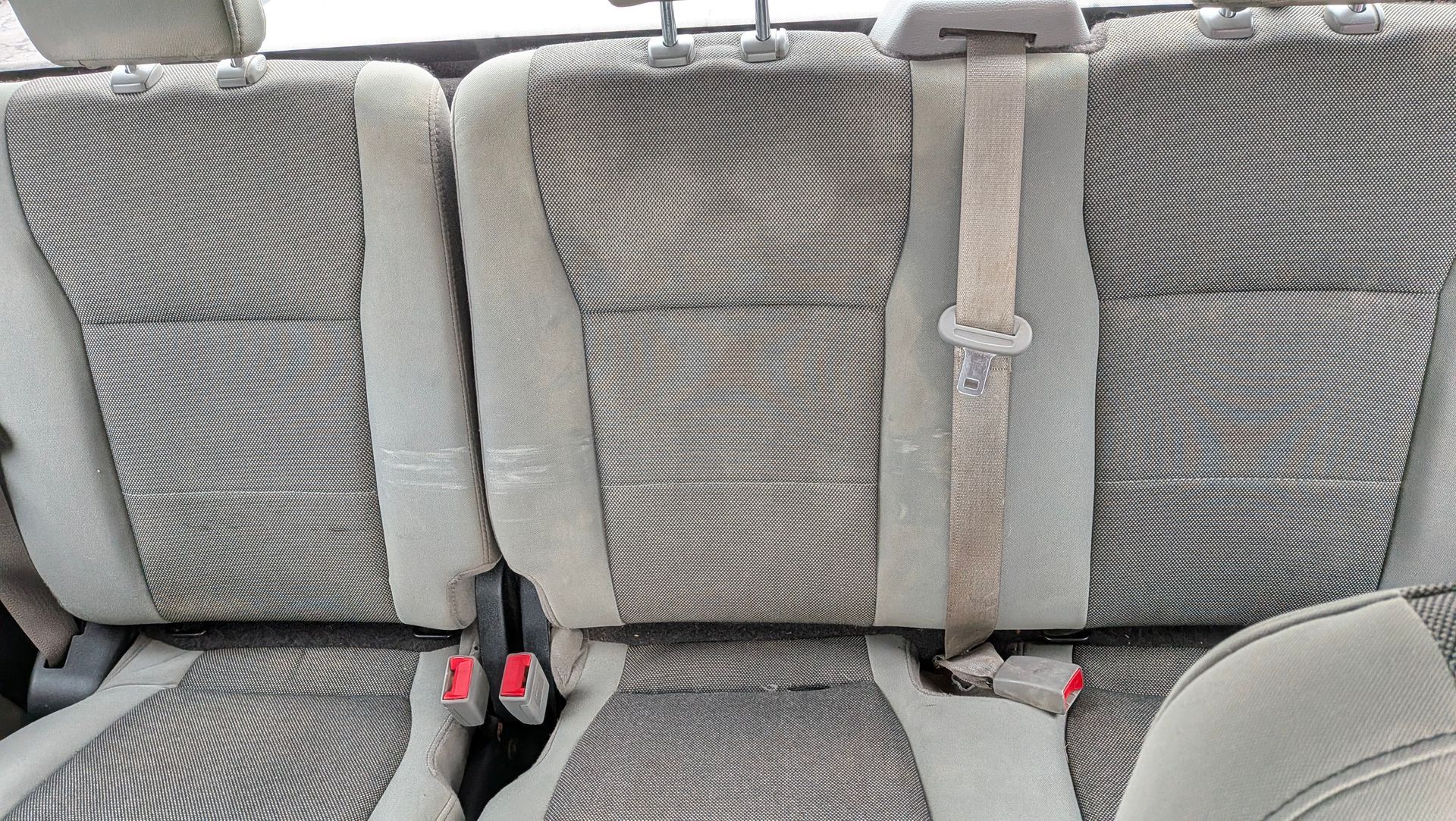 Beige and gray car backseat with three headrests and seatbelts.