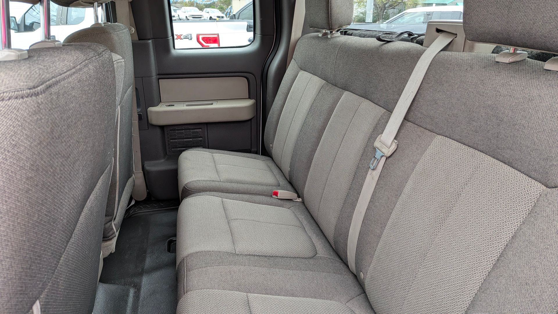 Back seat of a gray Ford F-150 truck with fabric upholstery, seatbelts, and a center console.