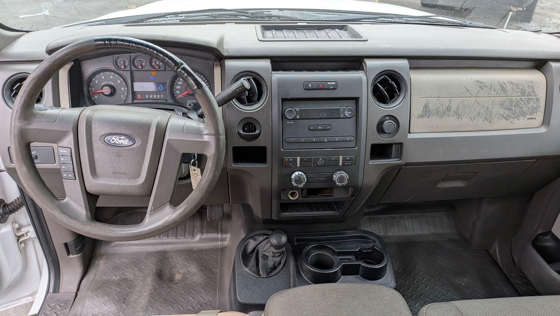 Ford F-150 truck interior: dashboard, steering wheel, radio, air vents, and center console. Dusty, gray interior.