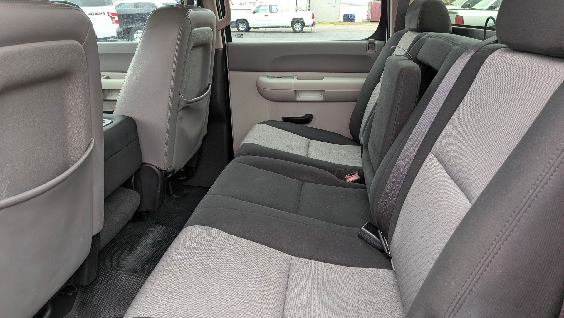 Interior view of a truck's back seat. Gray and black fabric seats, side panels, and seat belts.