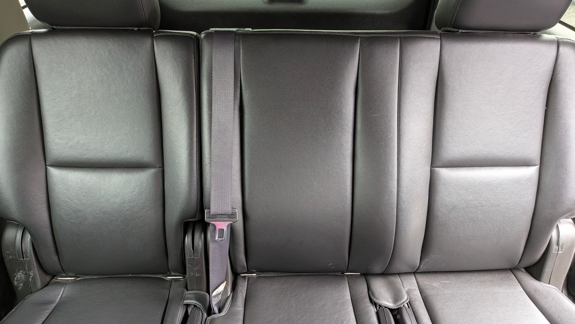 Black leather car seats with seatbelts in the middle row.