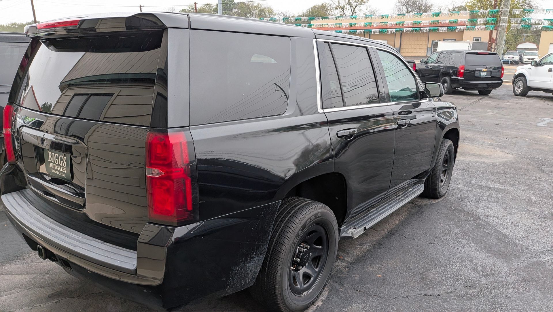 Black SUV with tinted windows, parked on a gravel lot near other vehicles.