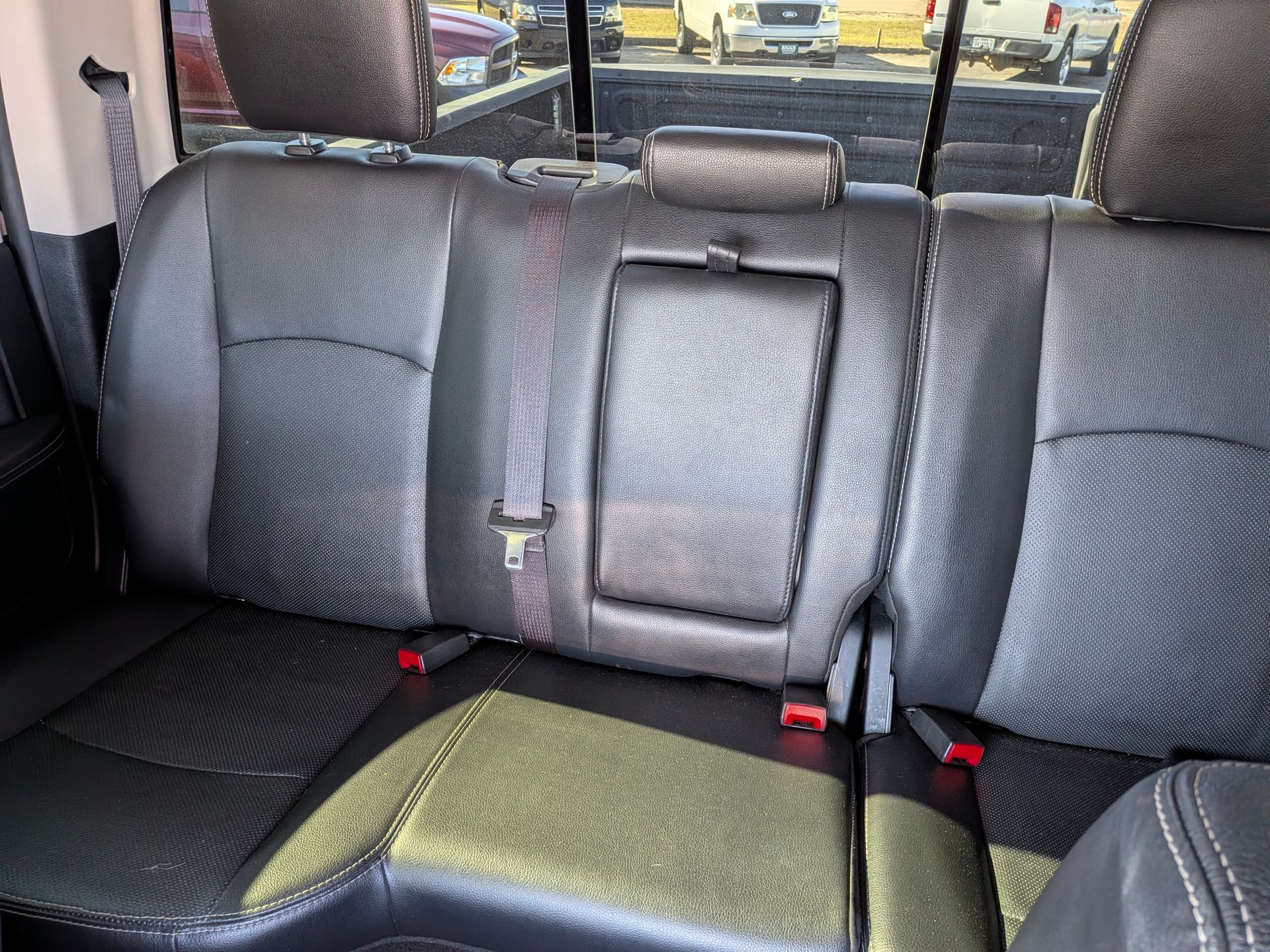 Black leather truck rear seats with center fold-down armrest, viewed from inside the cab.