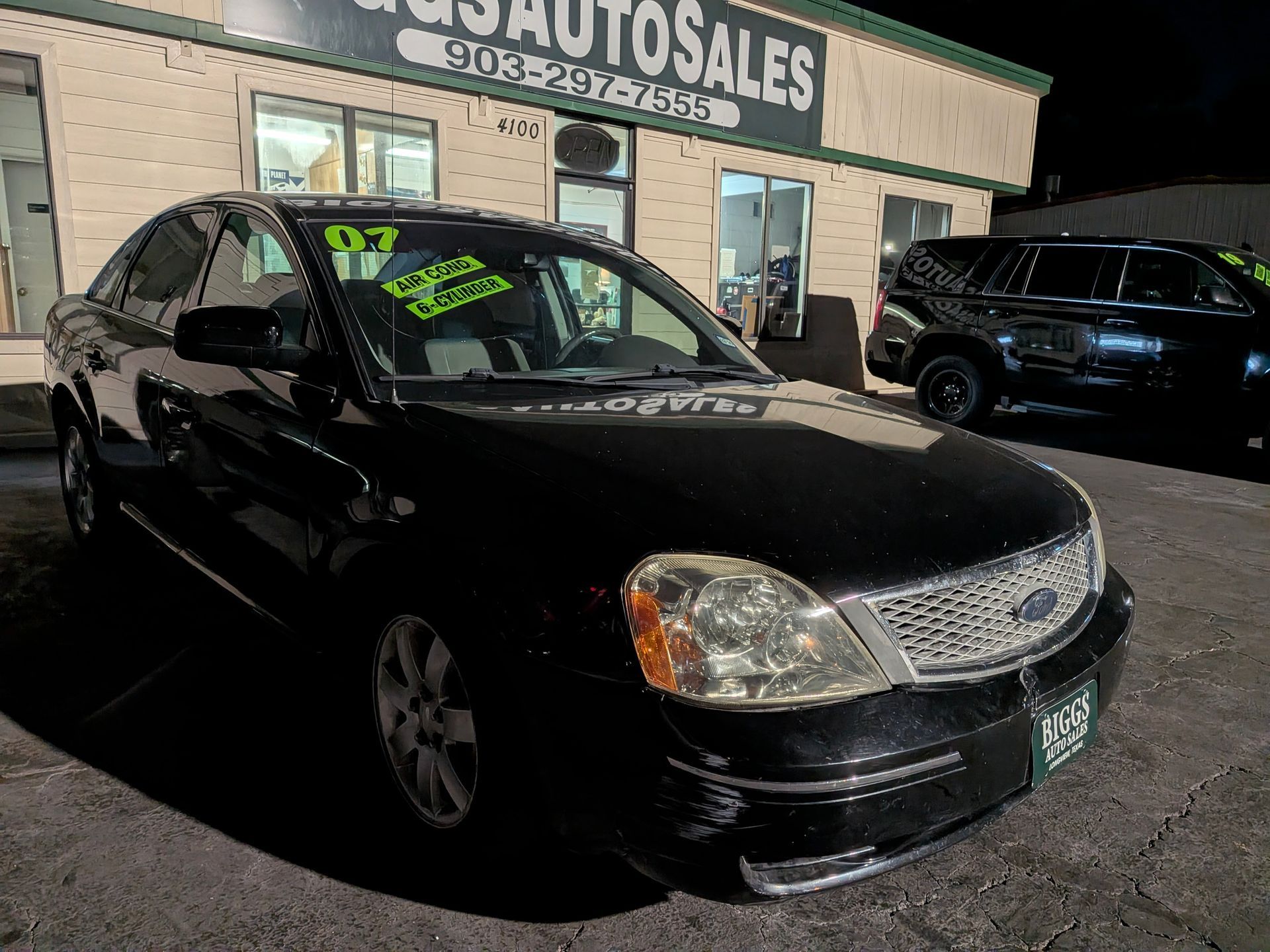 Black 2007 Ford Five Hundred sedan parked in front of a car dealership, with the business sign visible.