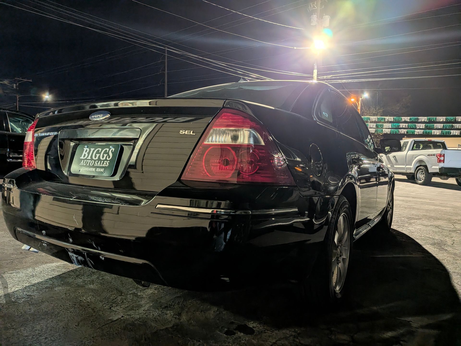 Black sedan parked outside at night. Tail lights lit. 