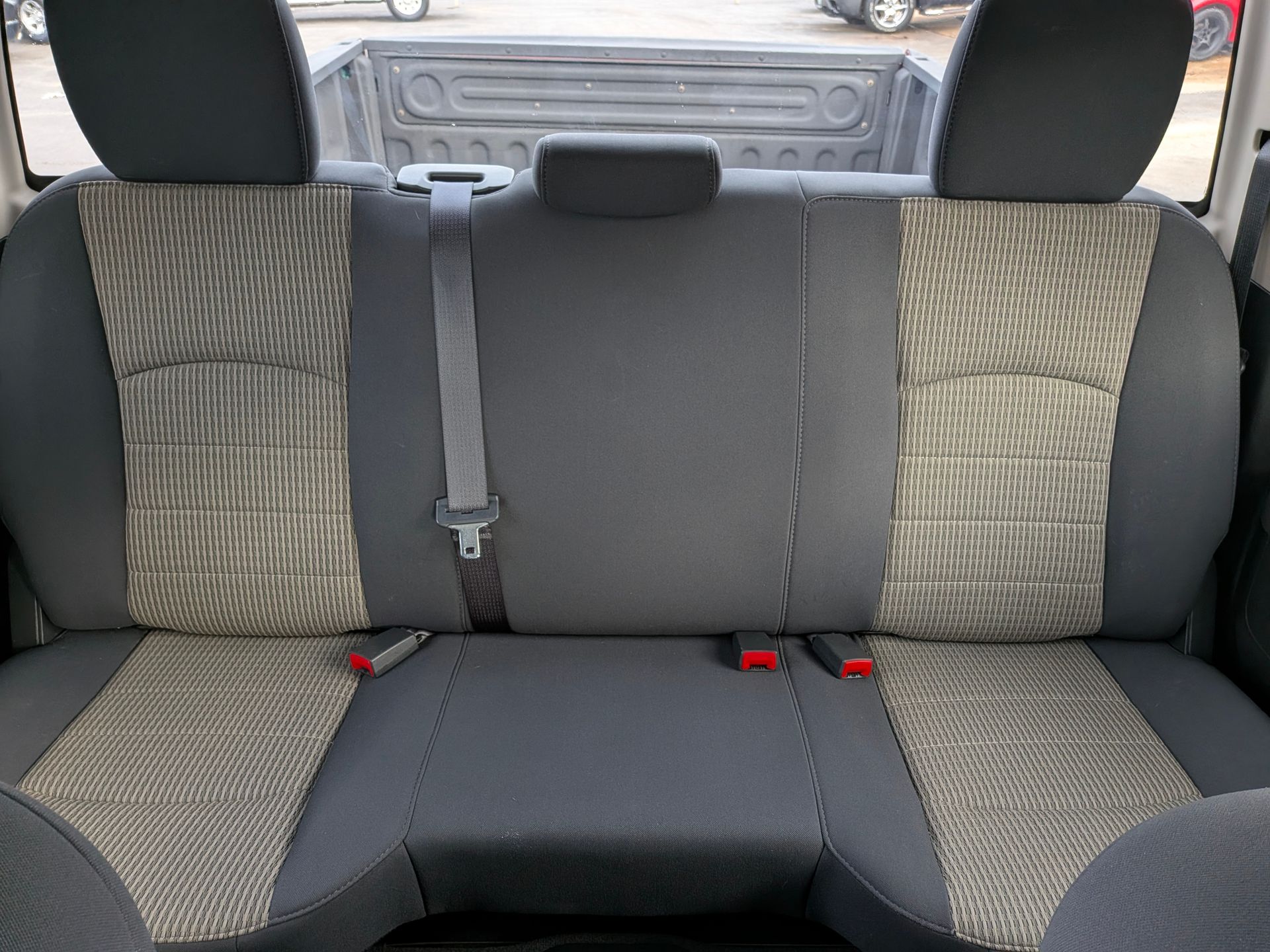 Gray and patterned truck back seat with three headrests and seatbelts.