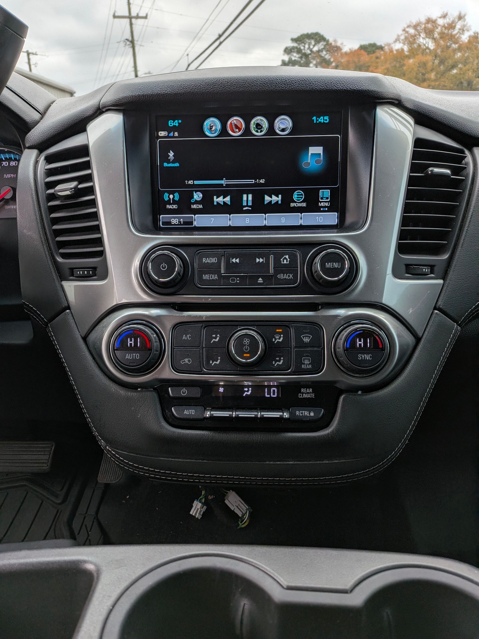 Car dashboard with infotainment screen, climate controls, and cup holders. Silver and black accents.