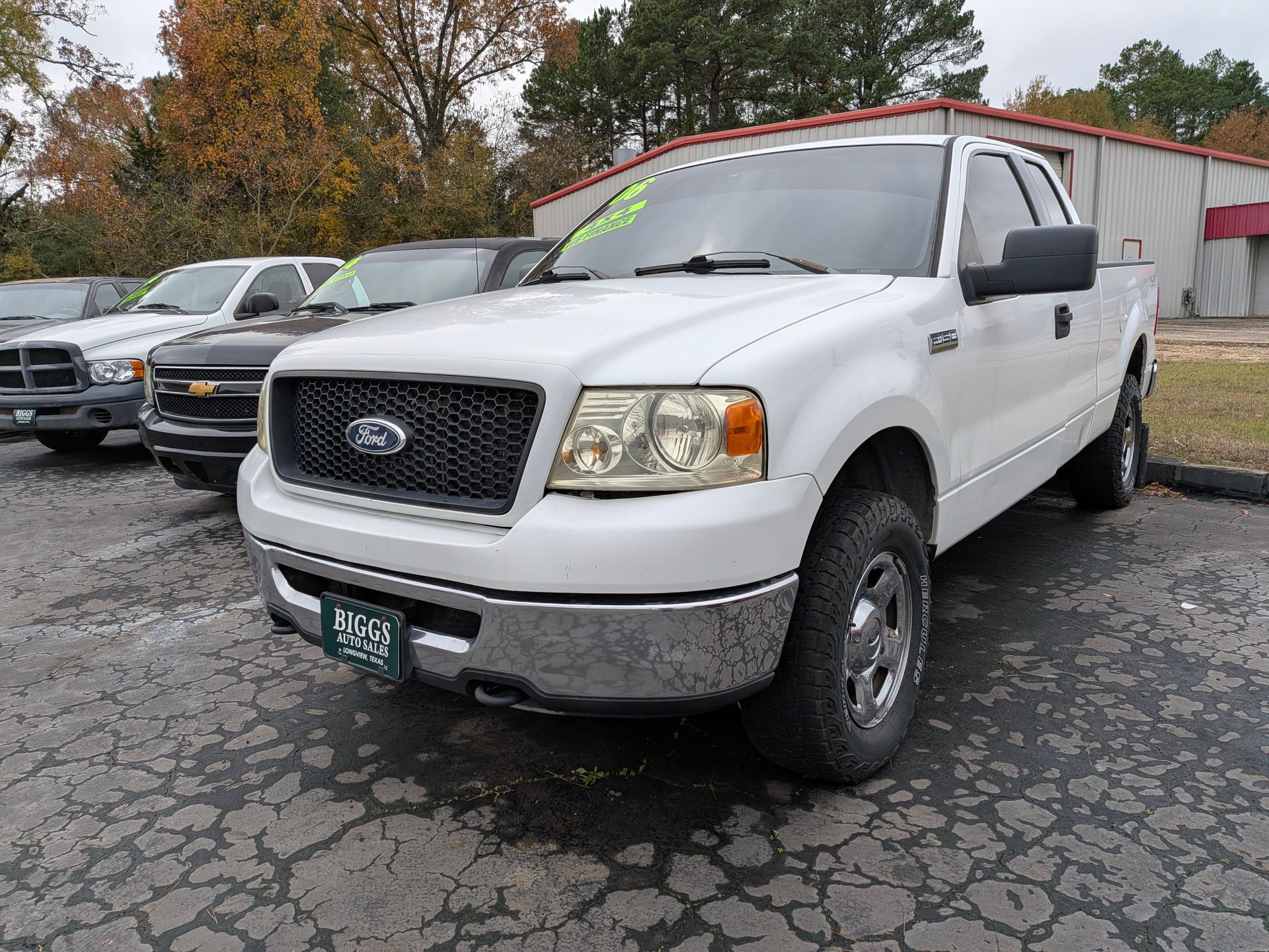 White Ford F-150 pickup truck parked on a lot, with other vehicles in the background. Cloudy day.