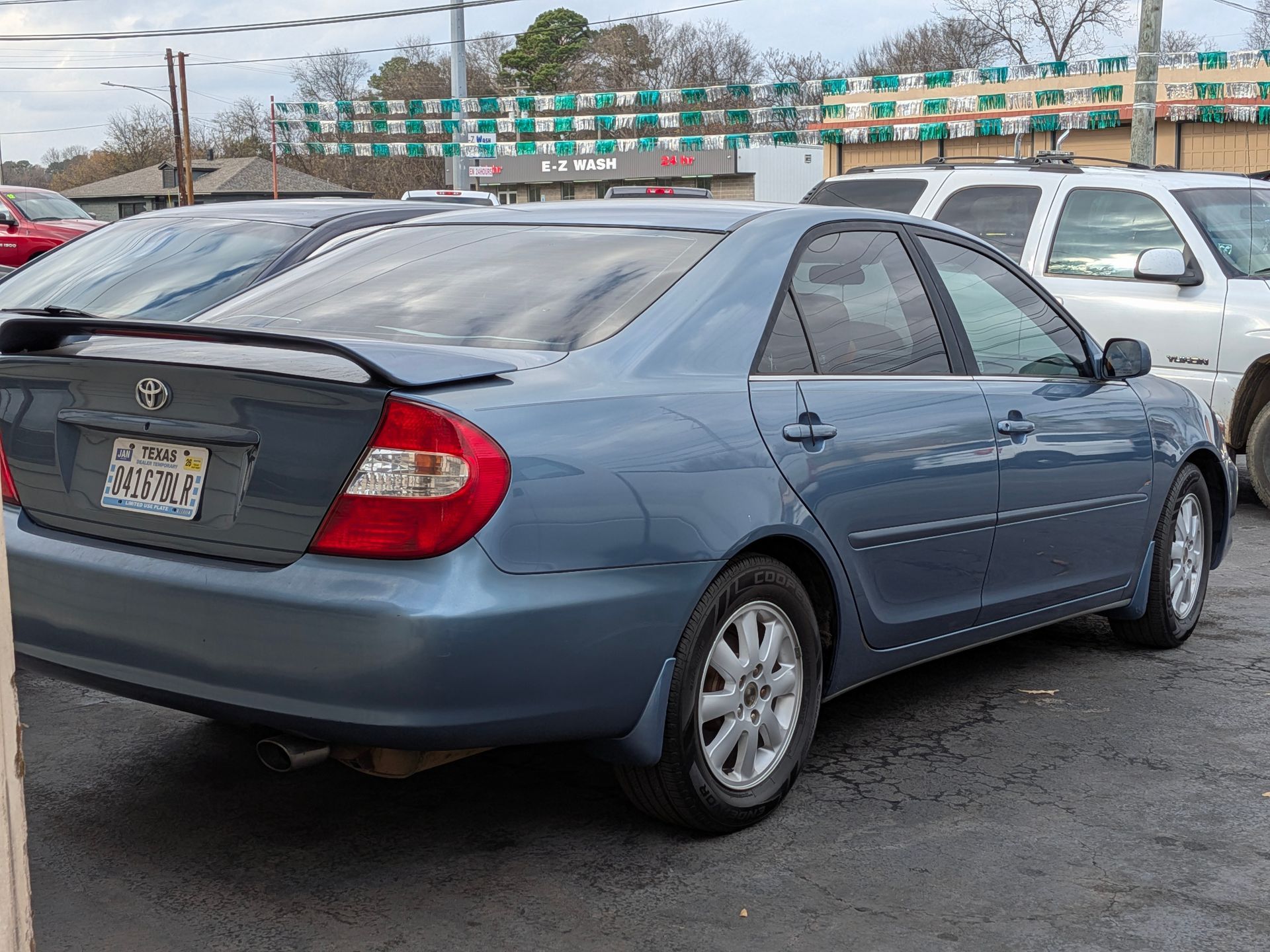 Blue Toyota Camry sedan with a rear spoiler, parked outside a dealership.