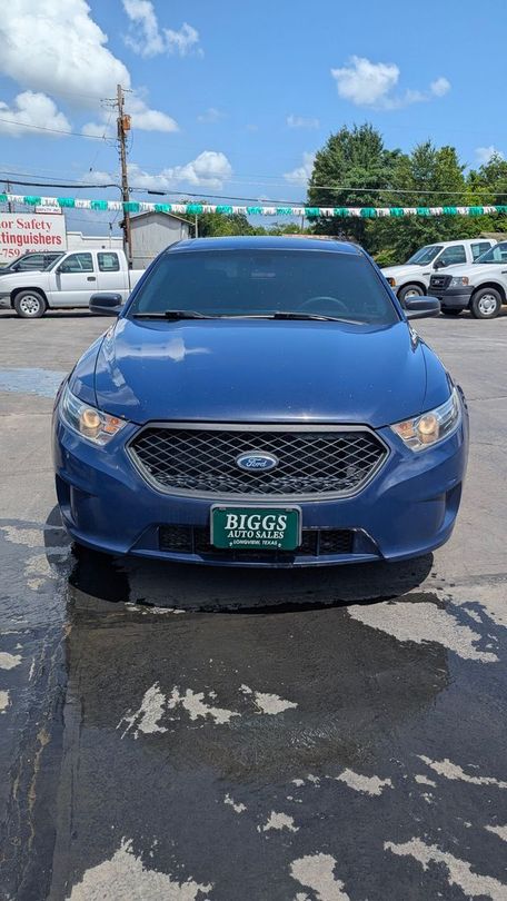 Blue Ford Taurus parked in front of a car dealership on a sunny day.