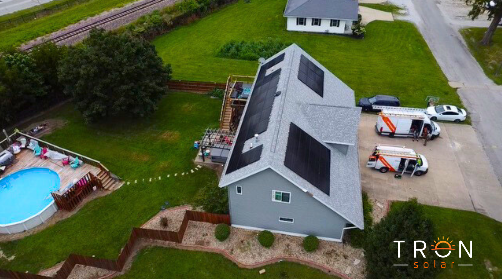 Aerial view of house with solar panels, pool, two orange vans parked, and green lawn.