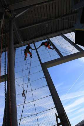 Two people are climbing a rope ladder in a building.