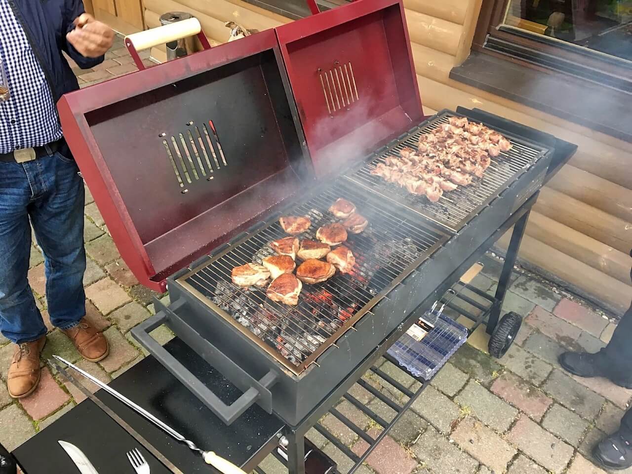 A man is standing next to a grill with meat on it.