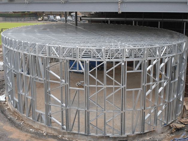 A large metal structure is being built on top of a dirt field.