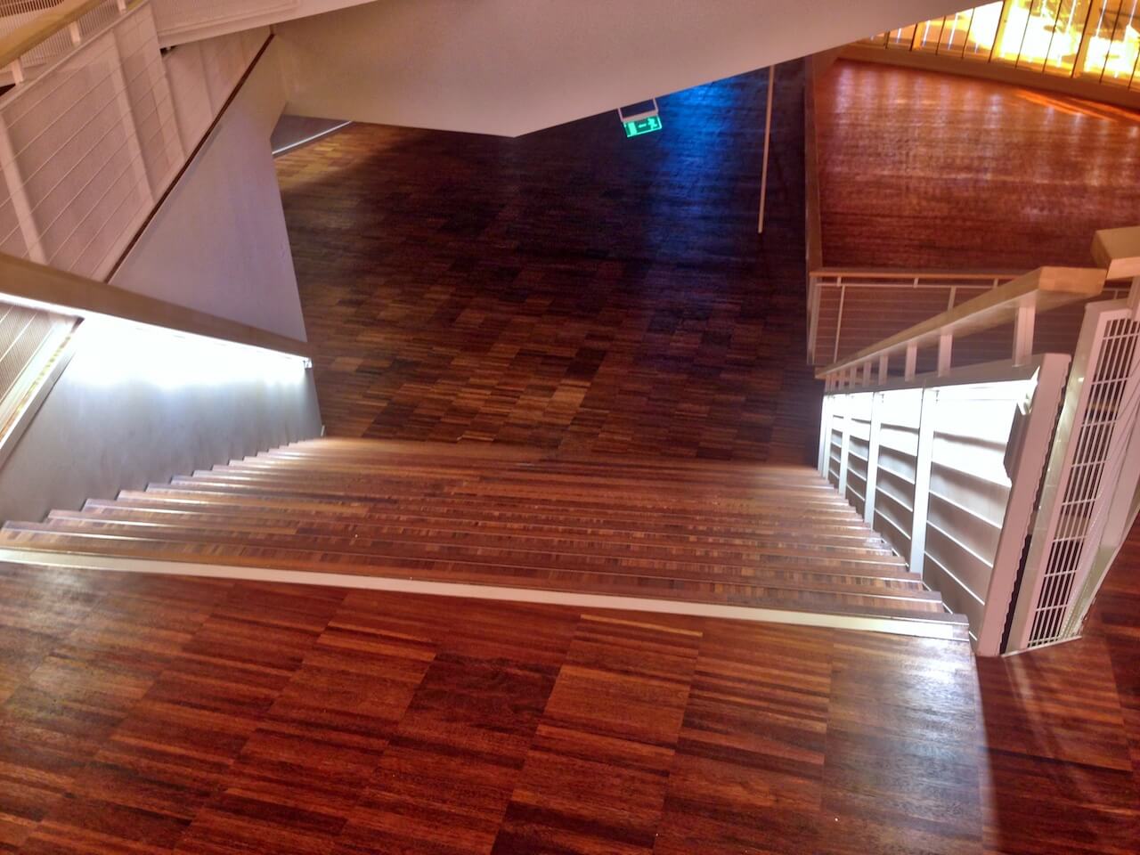 A staircase with a wooden floor and a green exit sign