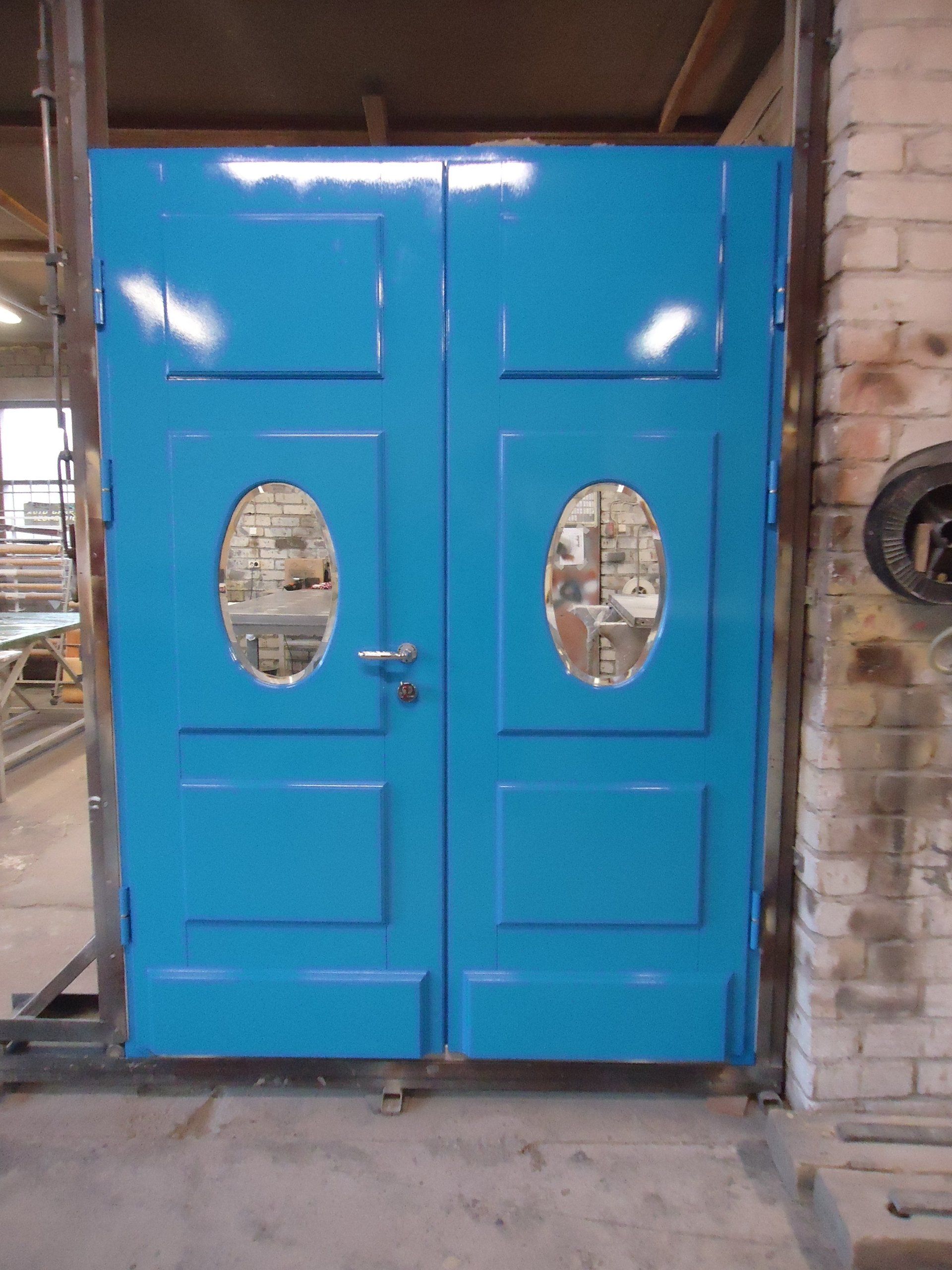 A blue door with oval windows is sitting in front of a brick wall