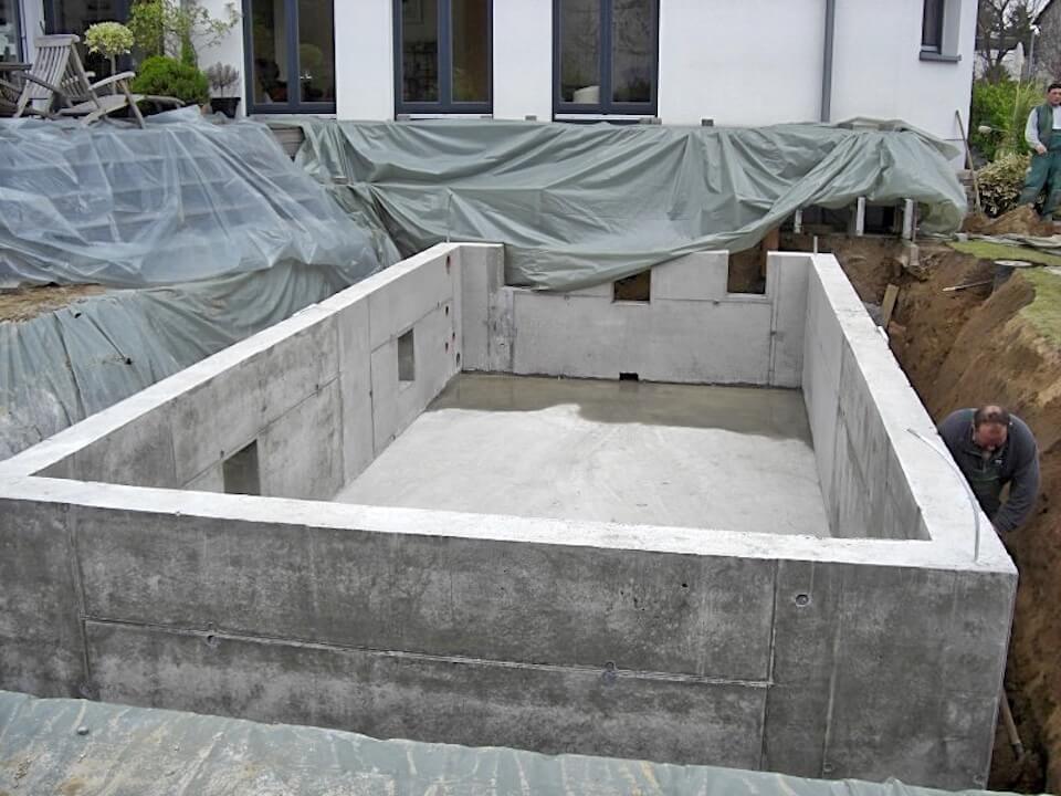 A man is working on a large concrete wall in front of a house.