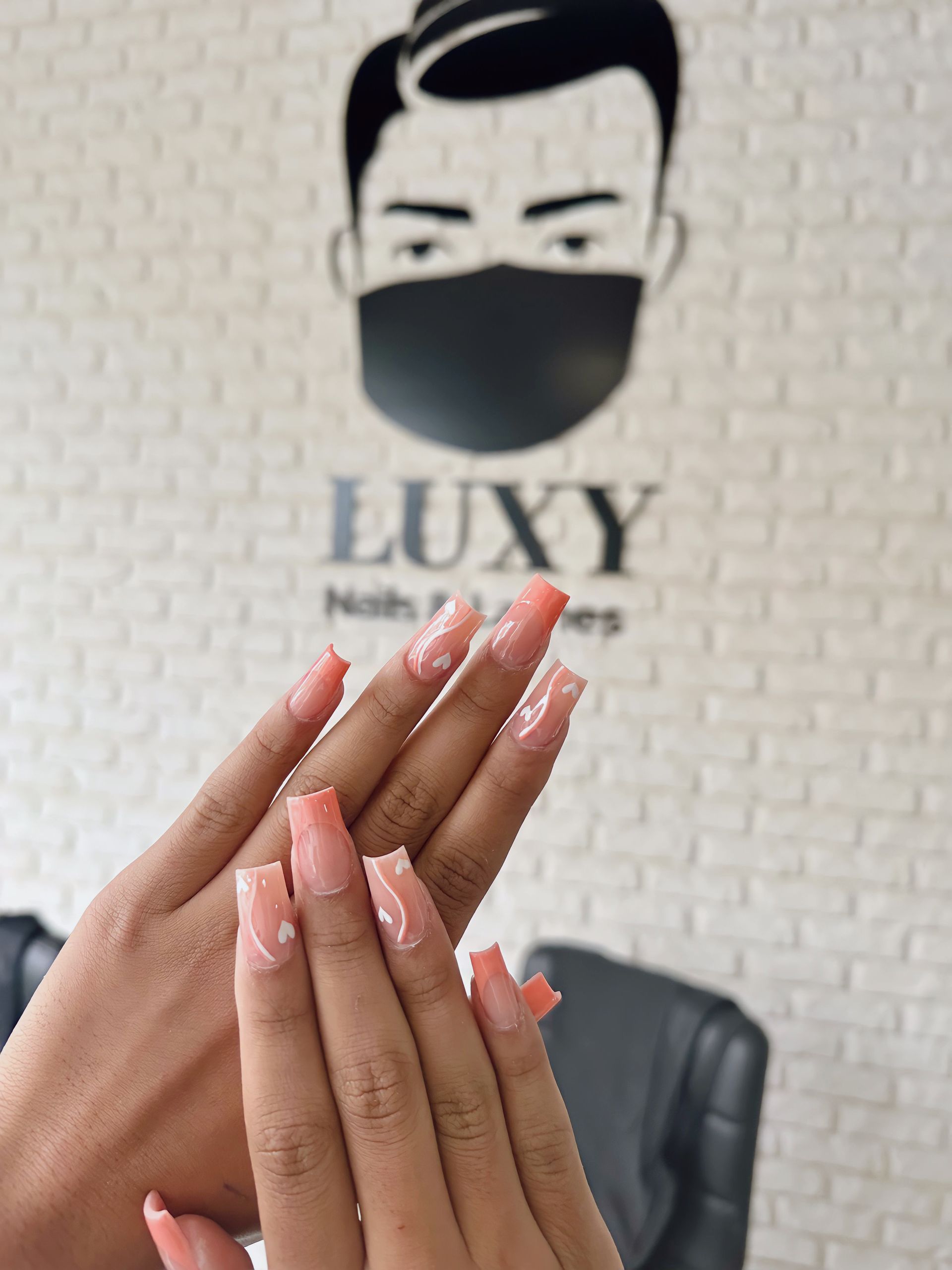 Eine Person hält ihre Nägel vor ein Schild mit der Aufschrift „Luxy“