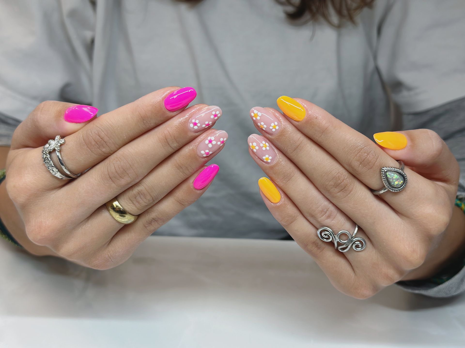 Die Hände einer Frau mit rosa und gelben Nägeln und Ringen daran.