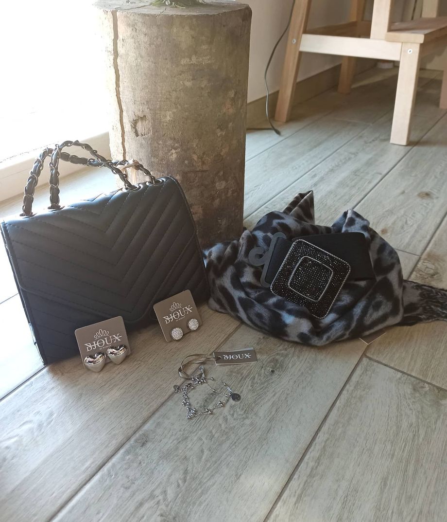 Una borsa, una sciarpa, degli orecchini e dei braccialetti sono su un pavimento di legno.