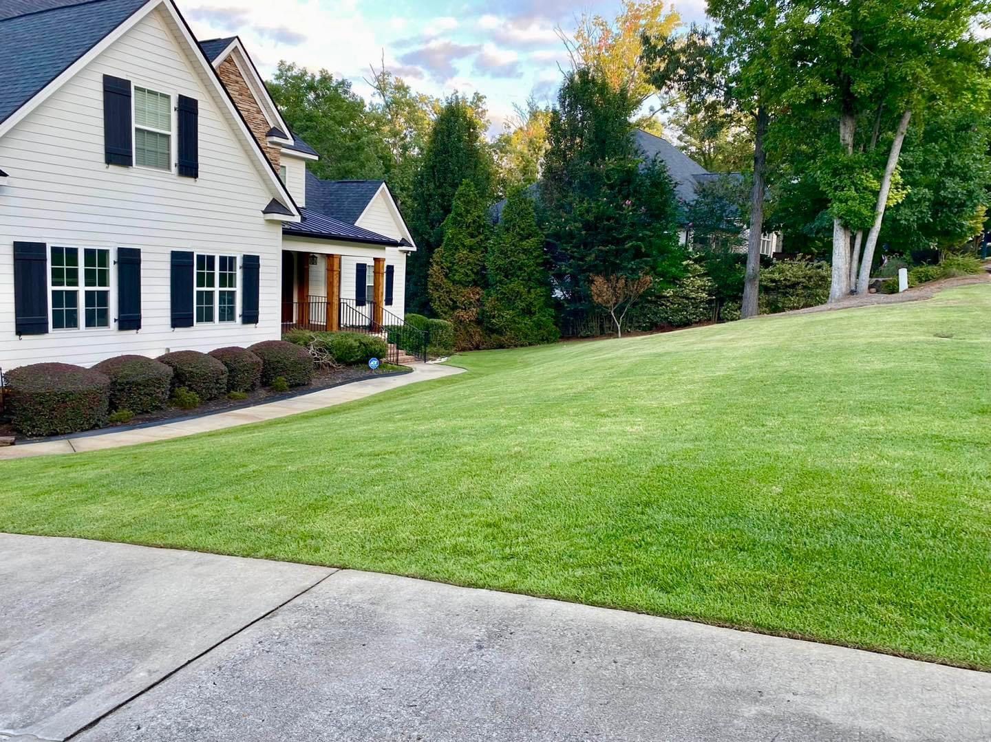 A white house with black shutters and a lush green lawn in front of it.