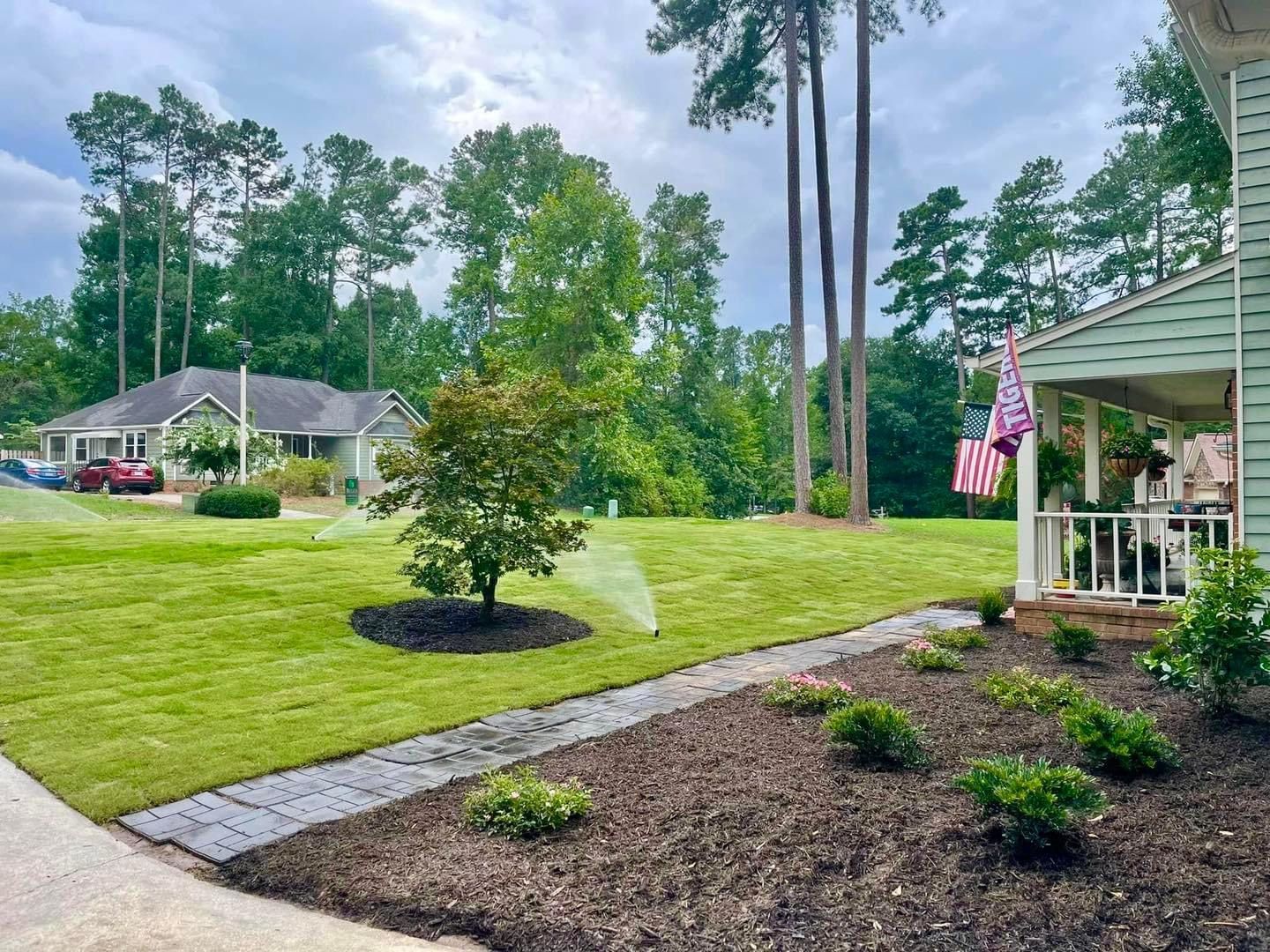 A lawn sprinkler is spraying water on a lush green lawn in front of a house.
