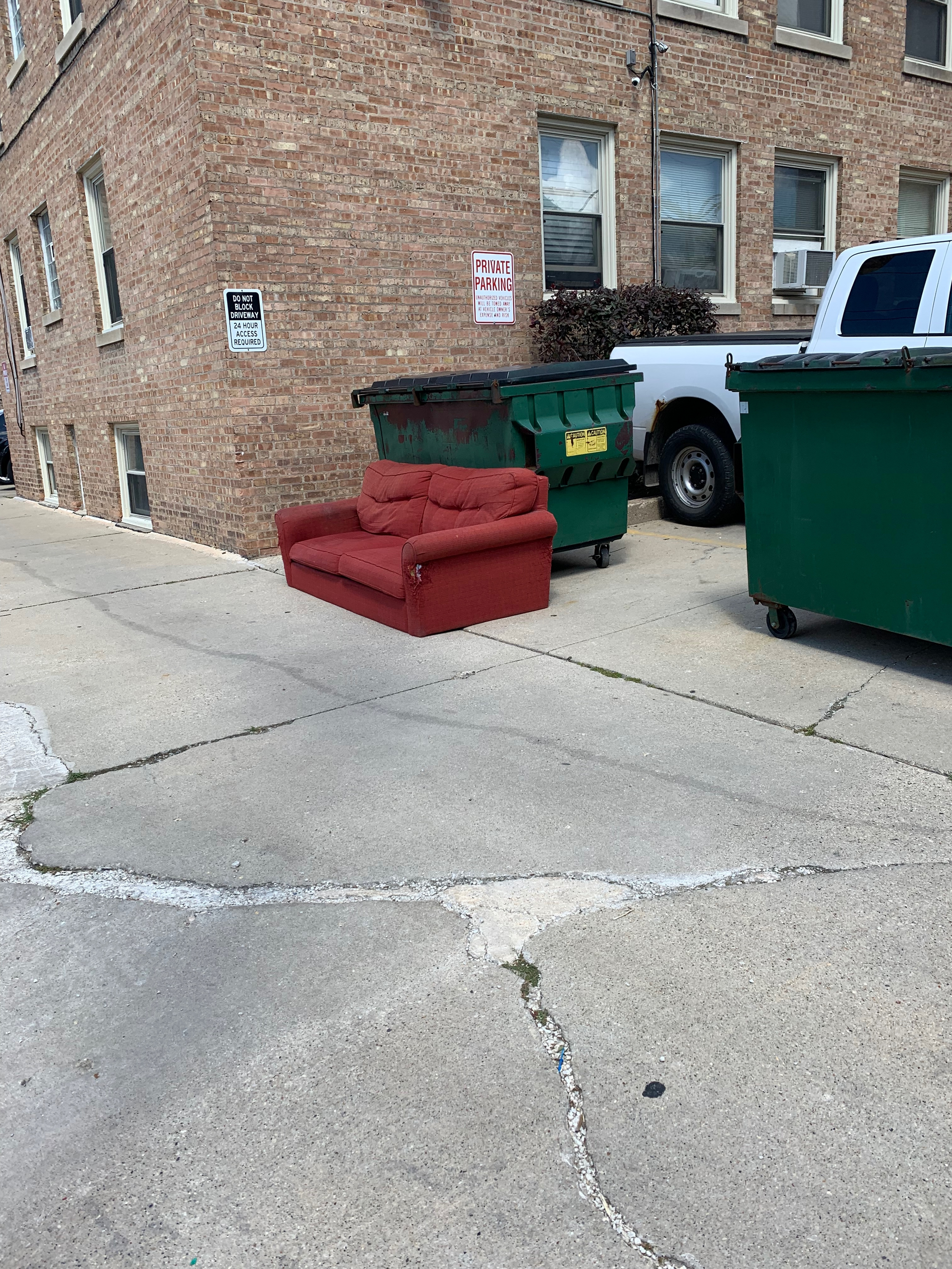 a red couch is sitting on the sidewalk next to a dumpster .