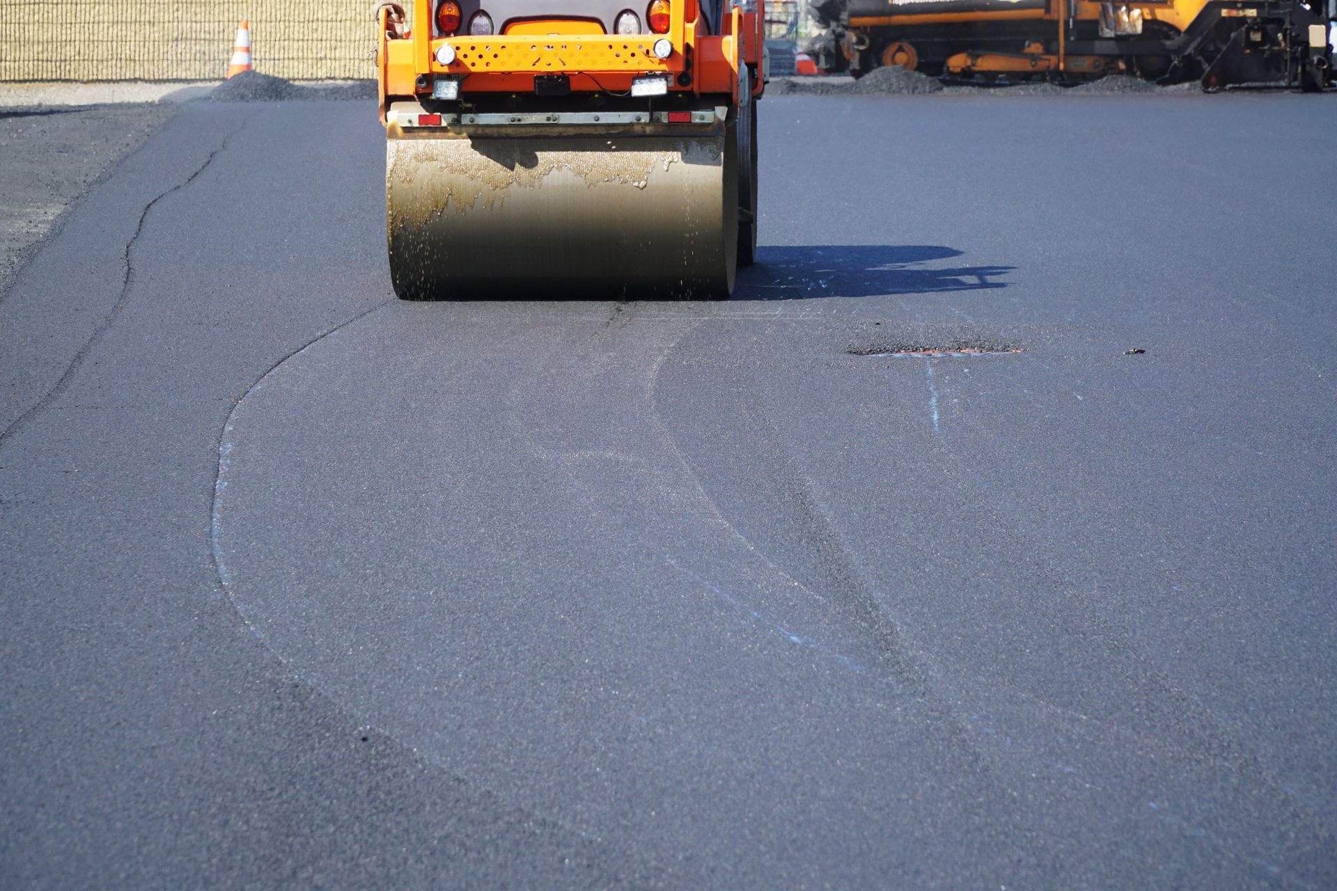 Asphalt roller compacting fresh black asphalt on a road surface.