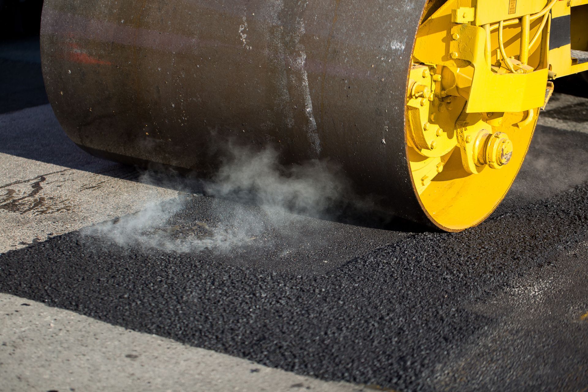 Yellow steamroller compacts fresh asphalt.