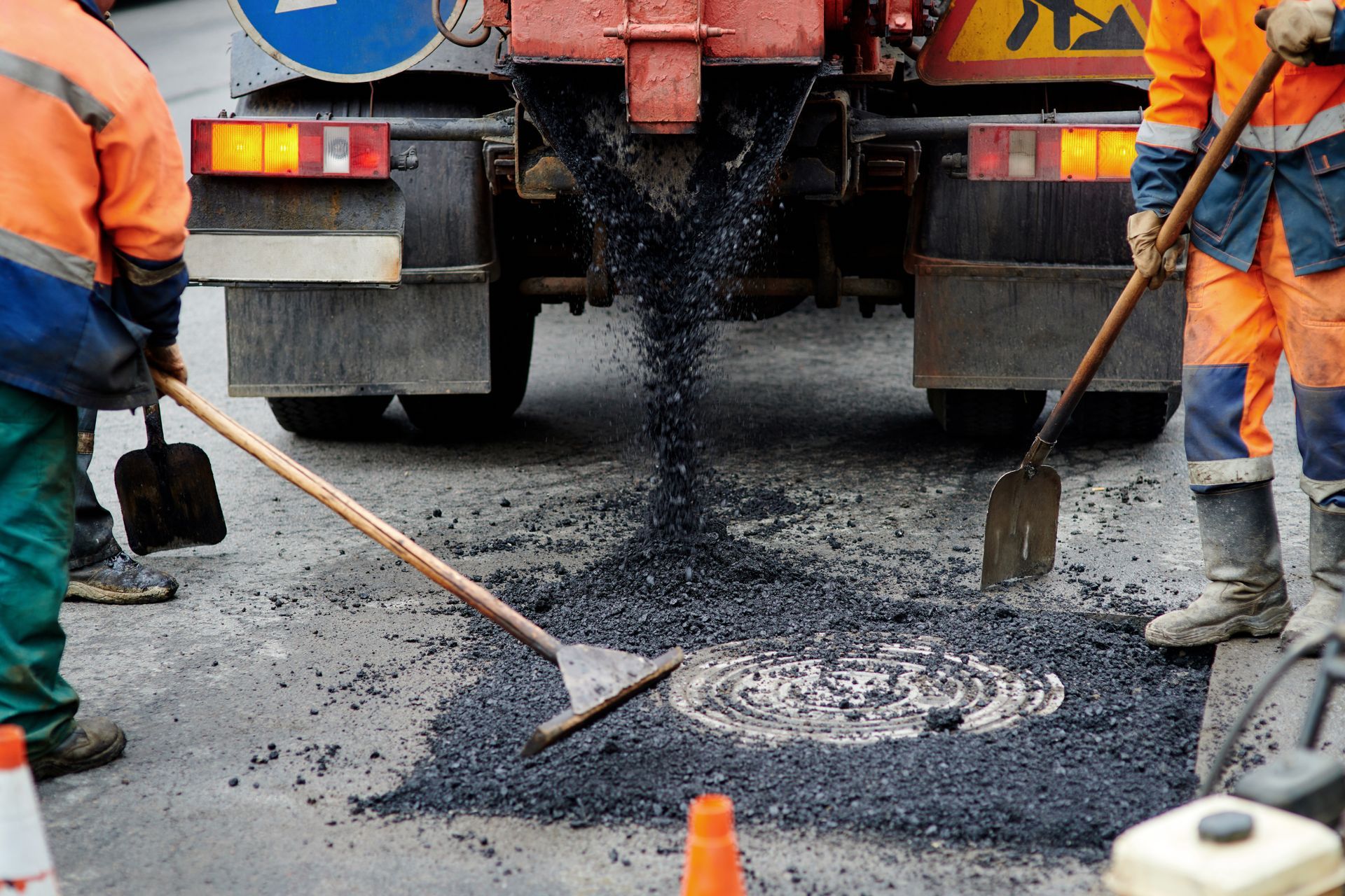 Road workers filling a pothole with asphalt from a truck, using shovels and rakes. Orange vests. Road workers filling a pothole with asphalt from a truck, using shovels and rakes. Orange vests.