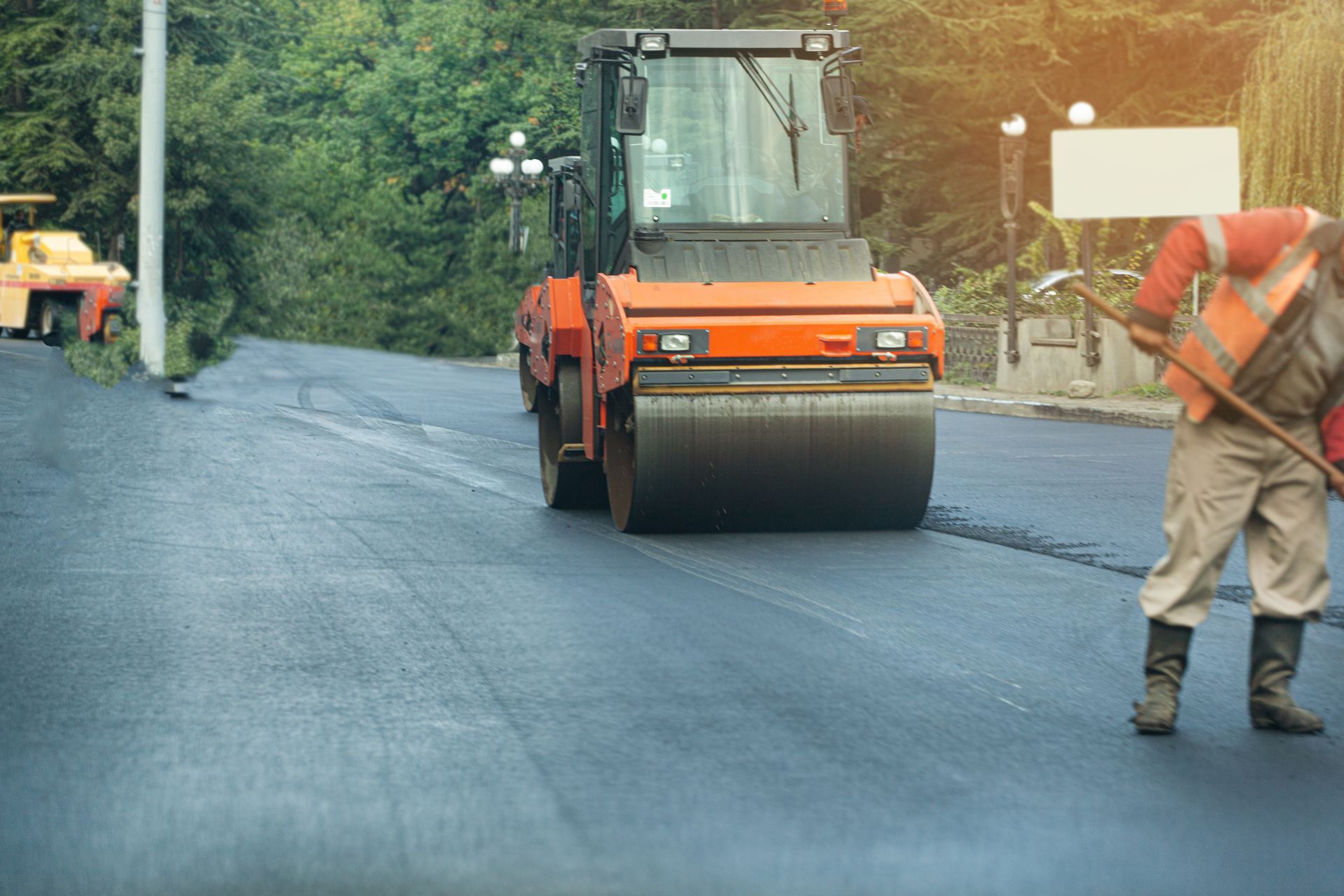 Road construction: Asphalt roller compacts fresh pavement as worker guides.