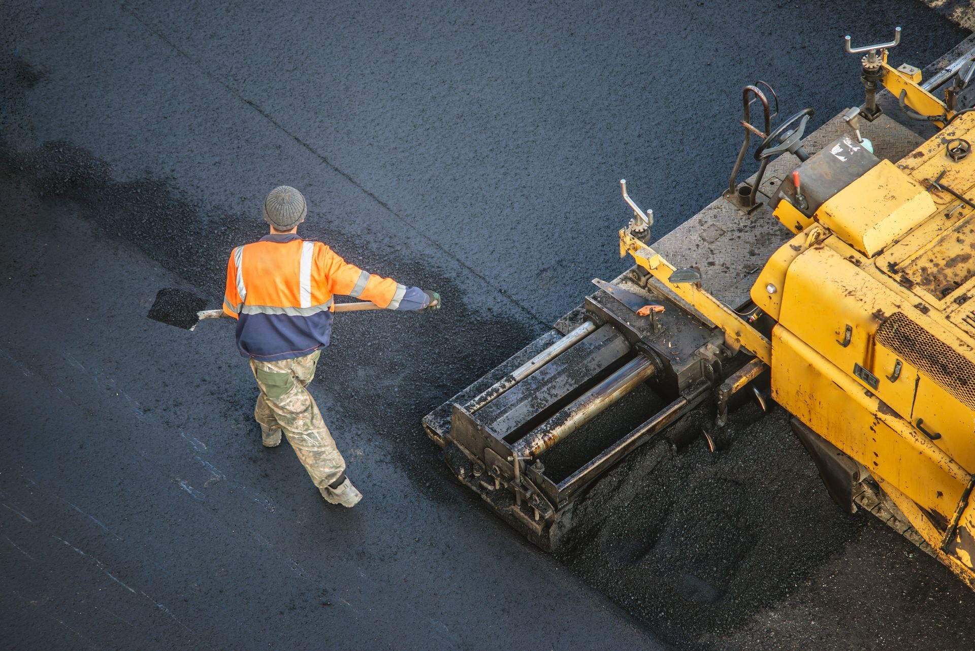 Worker with shovel beside asphalt paving machine.