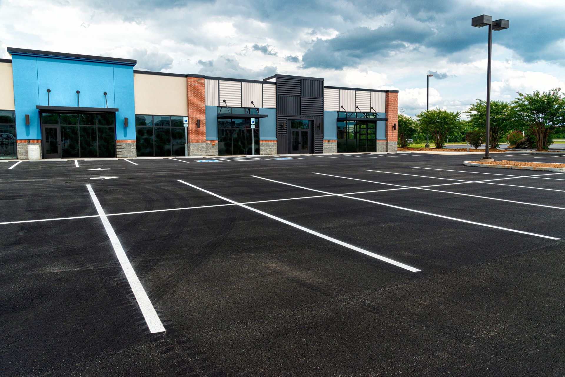 Empty parking lot in front of a strip mall with a cloudy sky.