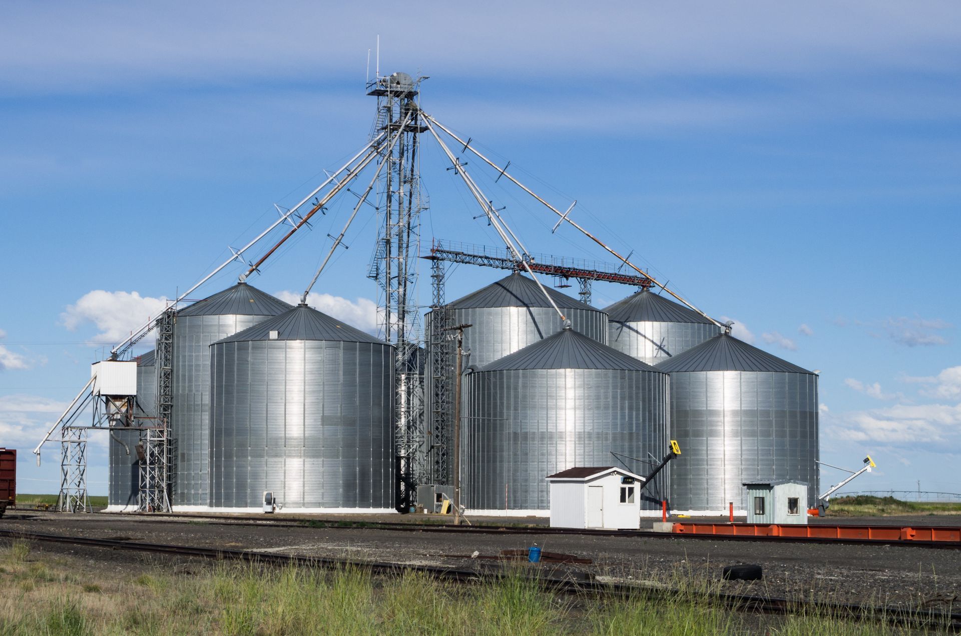 Grain silos on a rural landscape with blue sky. Metal structures with a small white building.