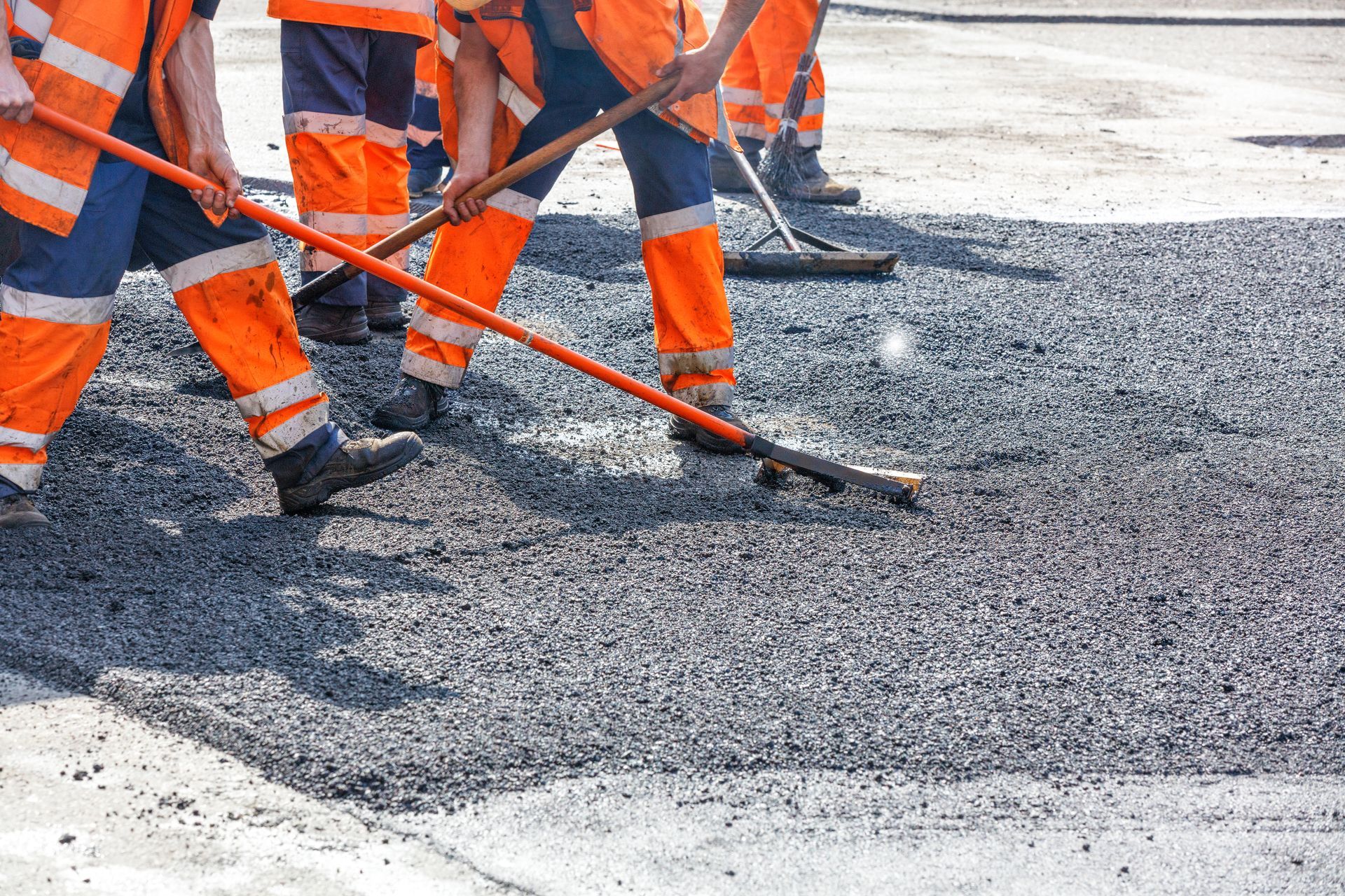 Construction workers in orange vests and pants spreading asphalt with rakes on a road.