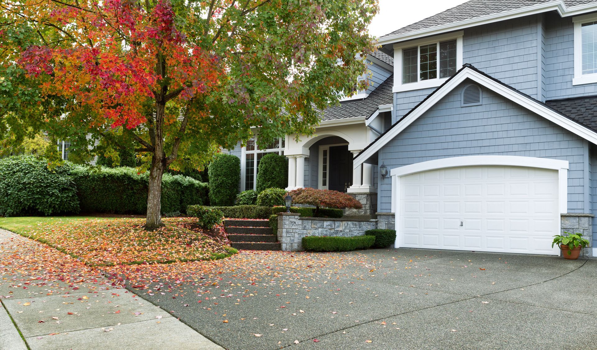 Blue house with white garage and red autumn tree in front.