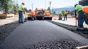 Road construction: Workers laying asphalt with shovels and machine.