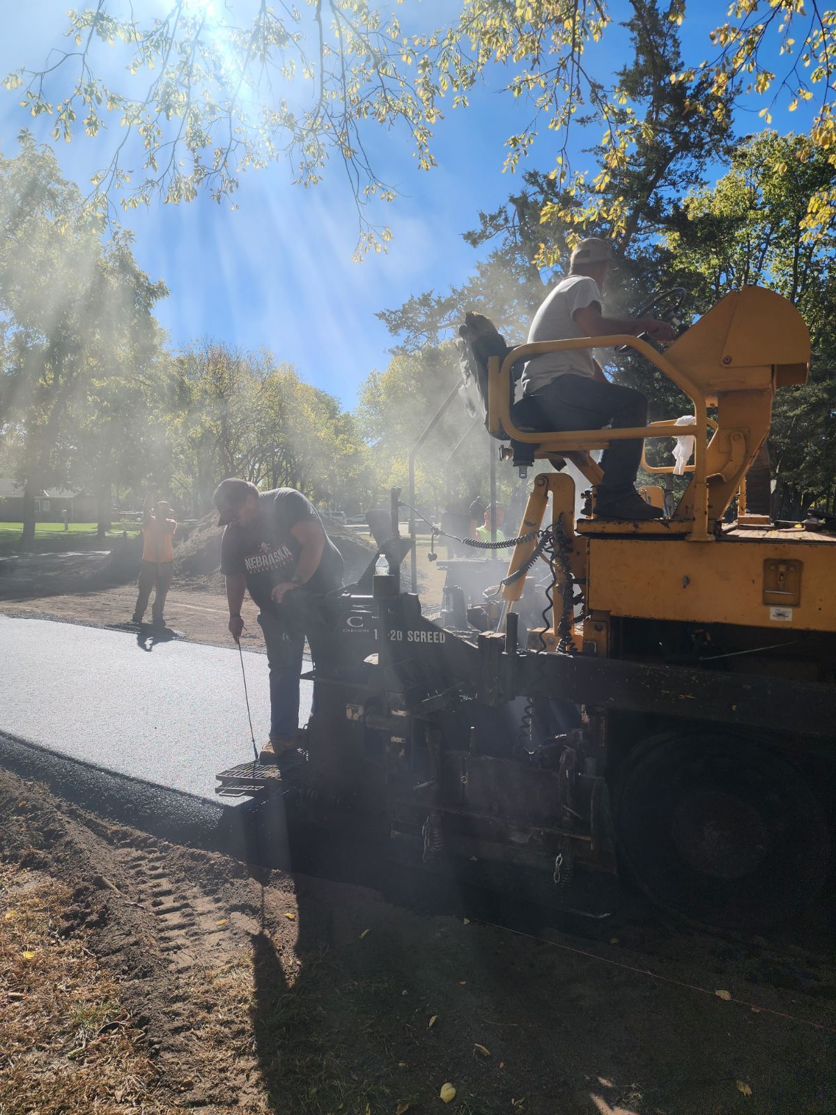 Asphalt paving crew using machinery on a sunny day.