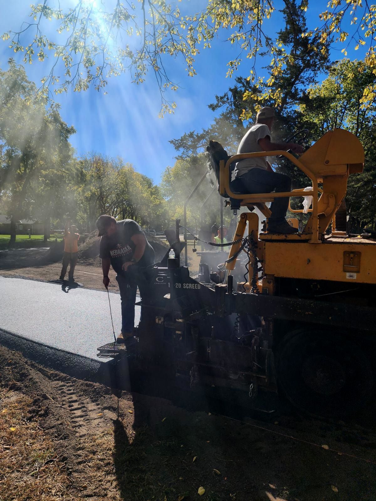 Road paving in progress. Workers operating asphalt paver on a sunny day.