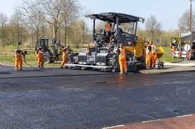 Road construction: Workers laying asphalt with shovels and machine.